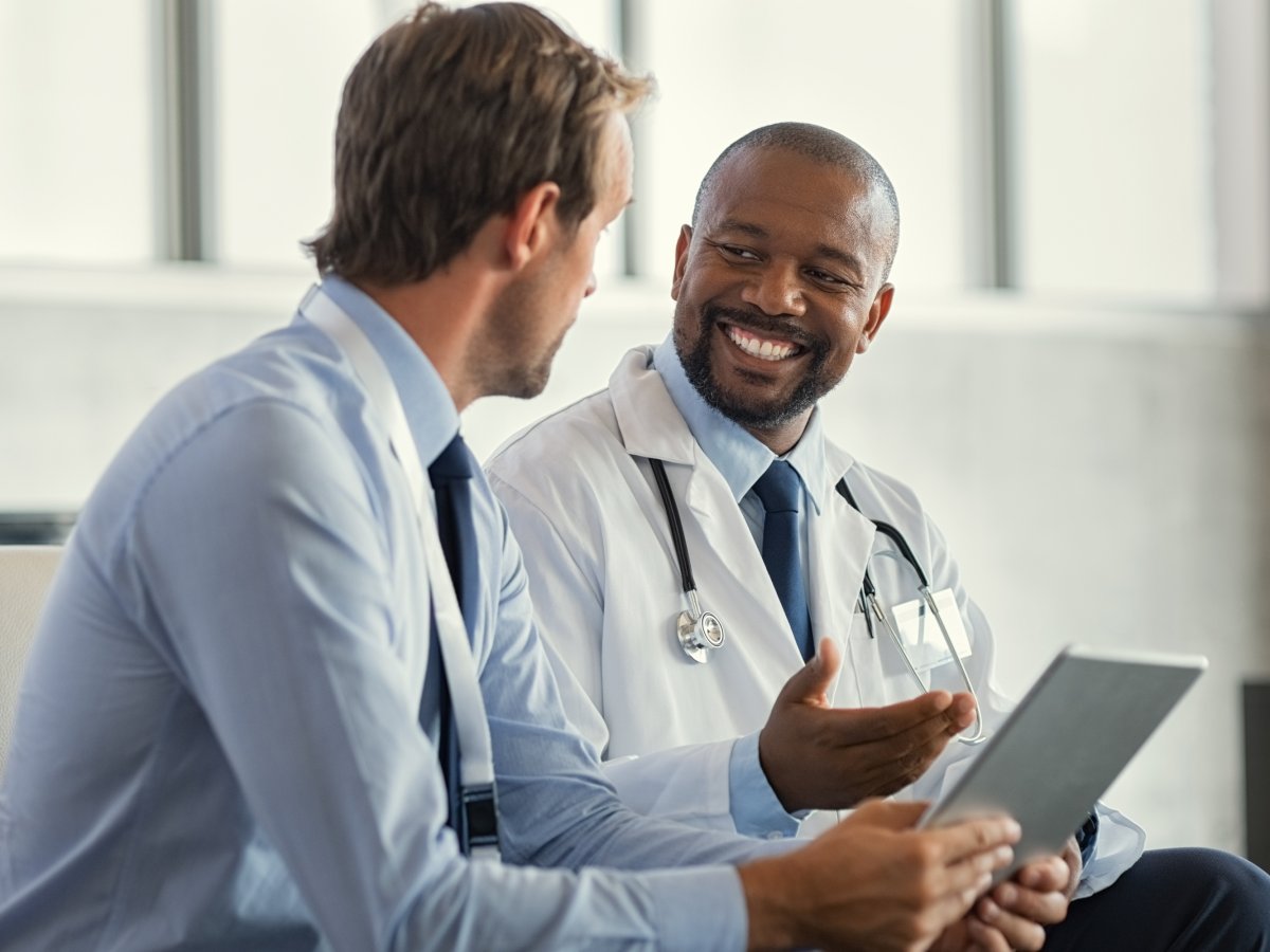 Smiling doctor going through something with a man on a tablet.