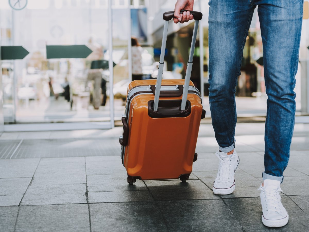 Person pulling an orange suitcase through an airport concourse.