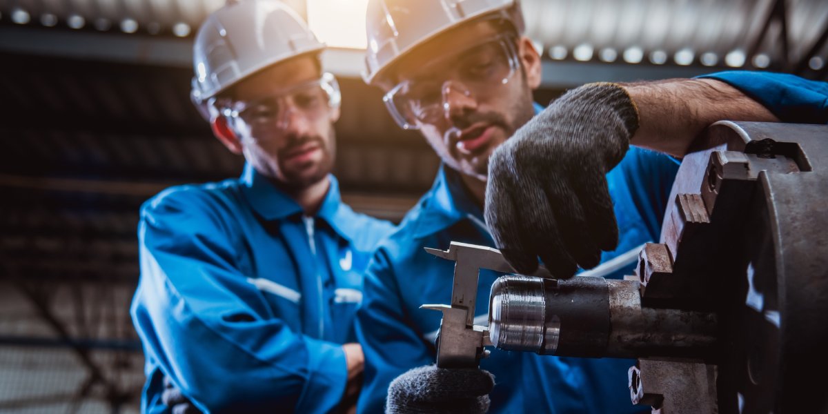 Two workers in hard hats measuring a workpiece in the workshop.