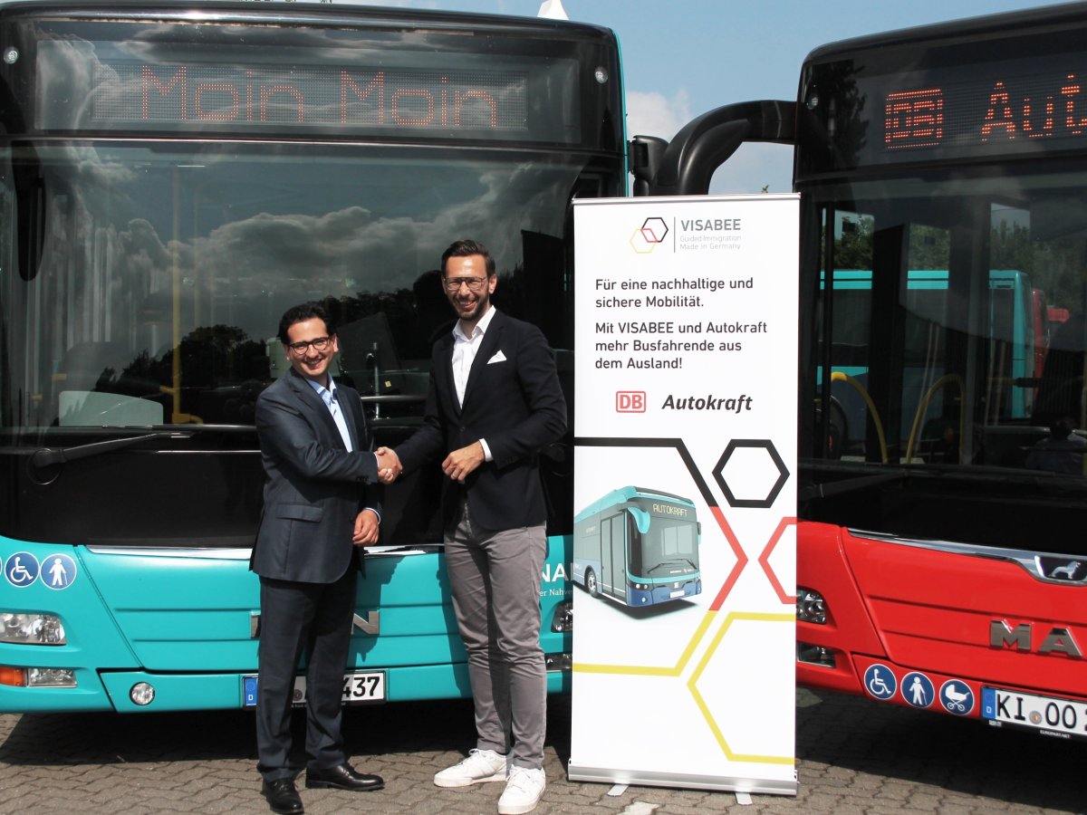 People standing between two city buses beside a display with the VISABEE and Autokraft logos.