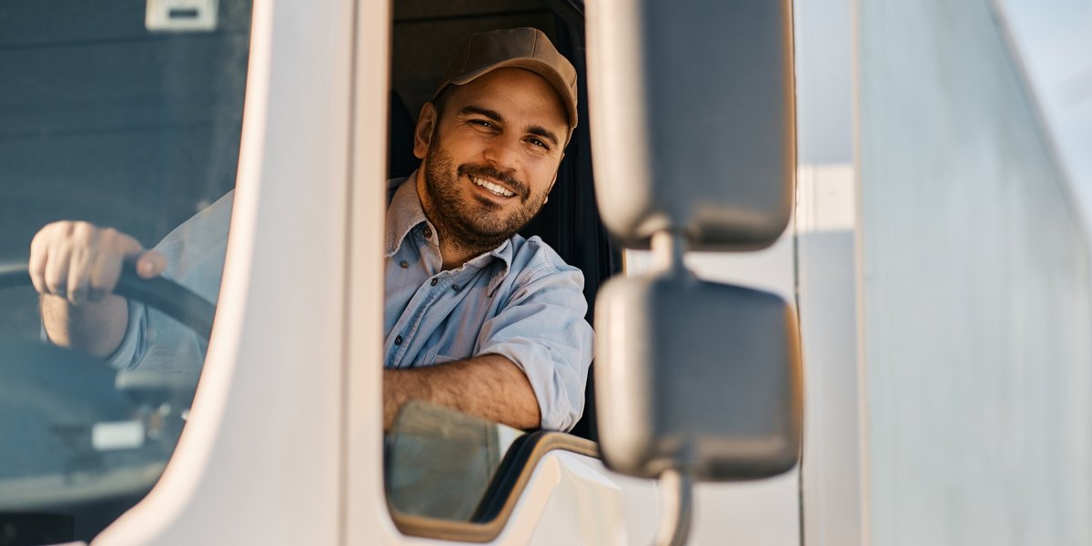 Smiling truck driver looking out of the side window while driving.